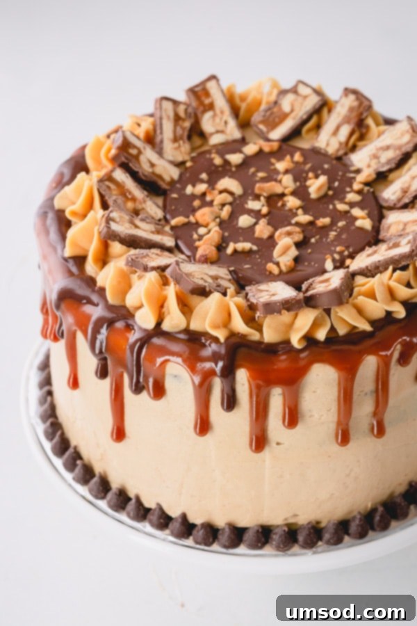 Chocolate Peanut Caramel Dream Cake 3 A whole Snickers layer cake, beautifully decorated with caramel sauce drips, chocolate ganache, and slices of Snickers bars on top.