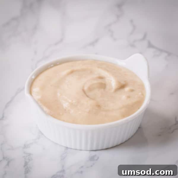 Dip into Delight: 5 Mouthwatering Sauce Recipes 11 A bowl of creamy tahini dip, garnished with a sprinkle of paprika and fresh parsley, served with carrot and cucumber sticks.