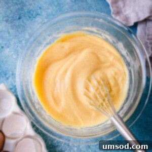 Velvety smooth pastry cream in a clear glass bowl, with a whisk nearby ready to incorporate into delicious desserts.
