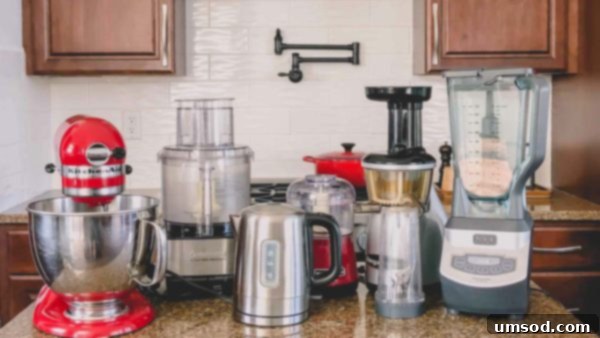 Small Kitchen Appliances I Can't Live Without 2 A collection of essential small kitchen appliances including a KitchenAid stand mixer, Cuisinart food processor, electric water kettle, mini food chopper, juicer, and blender, neatly arranged on a kitchen counter.