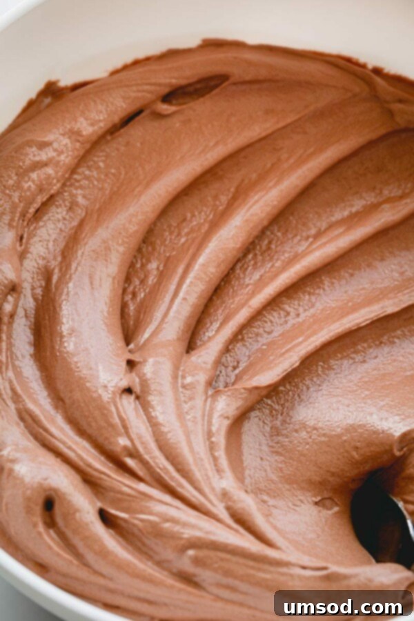 Chocolate Swiss meringue buttercream being skillfully piped onto a dessert, showing its smooth consistency