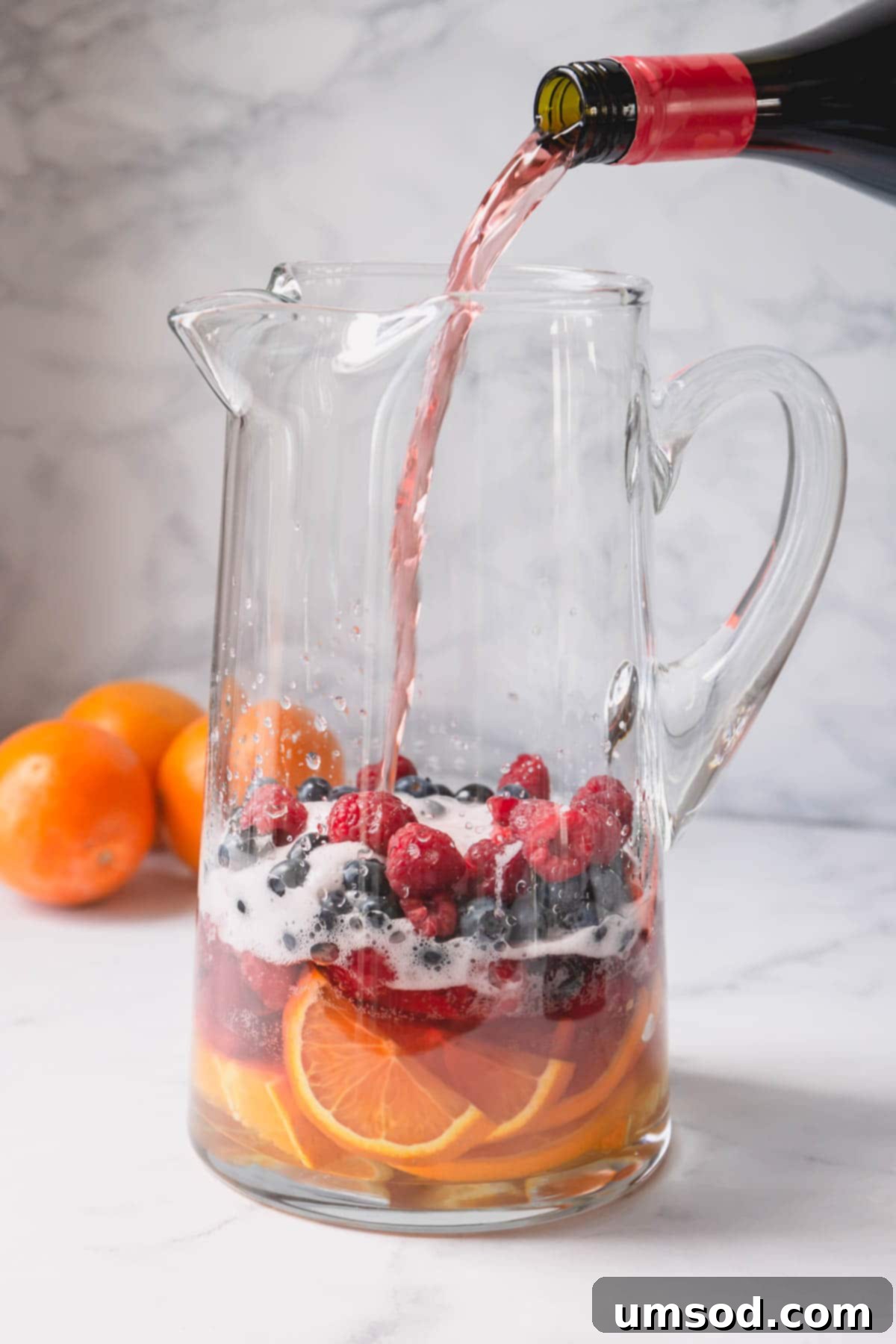 Sweet Summer Moscato Sangria 4 A pitcher of sliced oranges and berries with pink Moscato is pouring into it.
