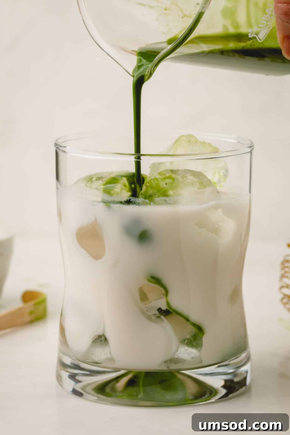 Mastering the Matcha Latte 11 Pouring vibrant green matcha paste into a glass filled with ice and creamy milk, creating a visually appealing layer.