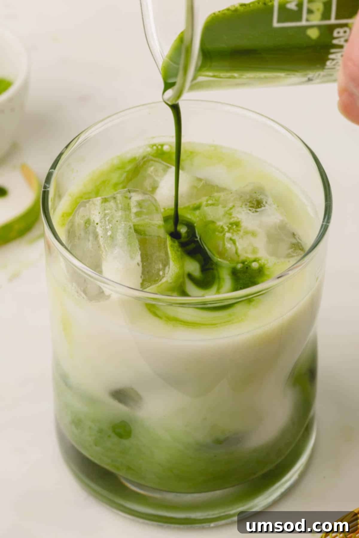 Mastering the Matcha Latte 3 Preparing an iced matcha latte: vibrant green matcha paste being poured over ice and milk in a clear glass.