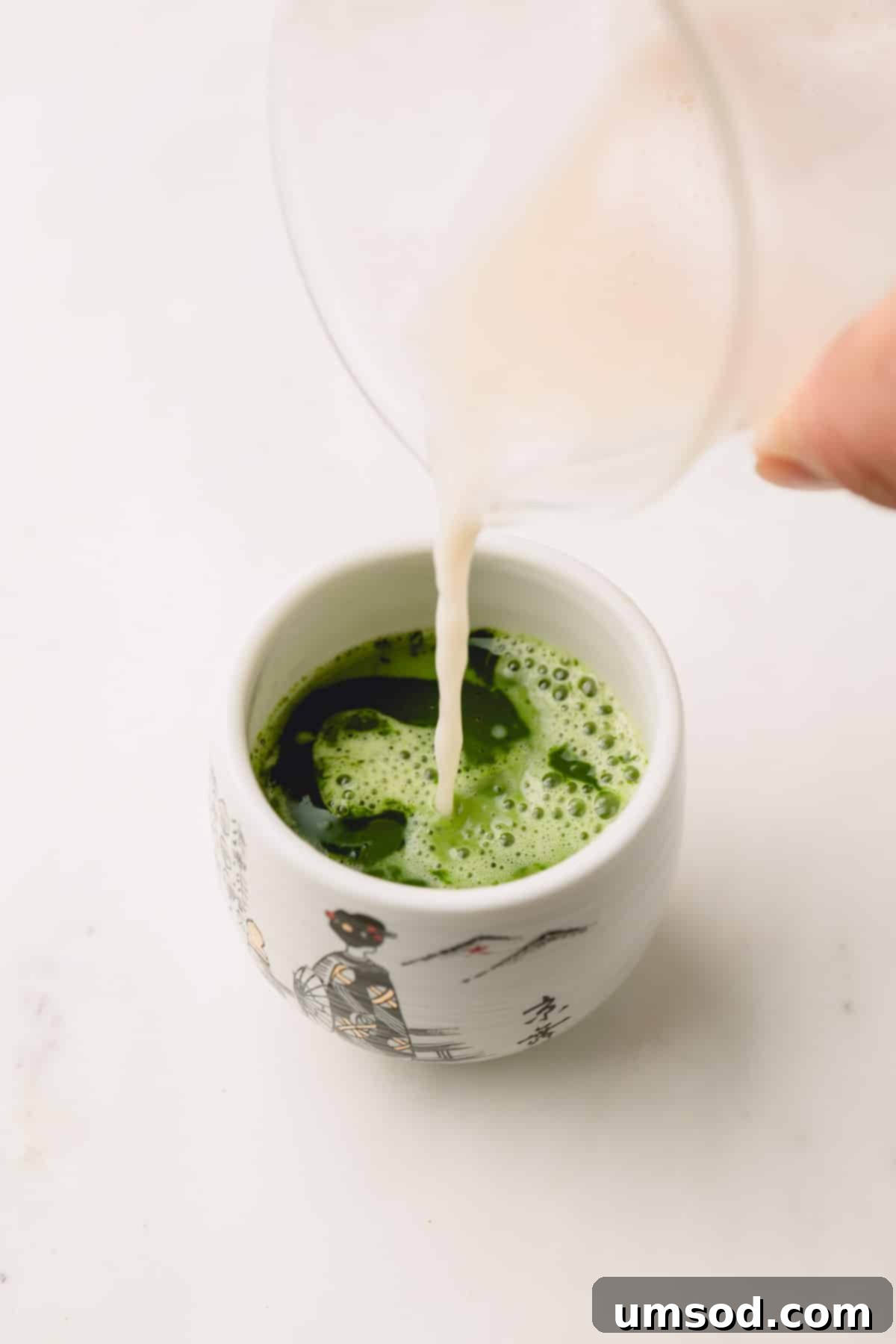 Mastering the Matcha Latte 9 Warm, frothed milk being gently poured into a small teacup containing the vibrant green matcha paste, creating a beautiful layered effect.