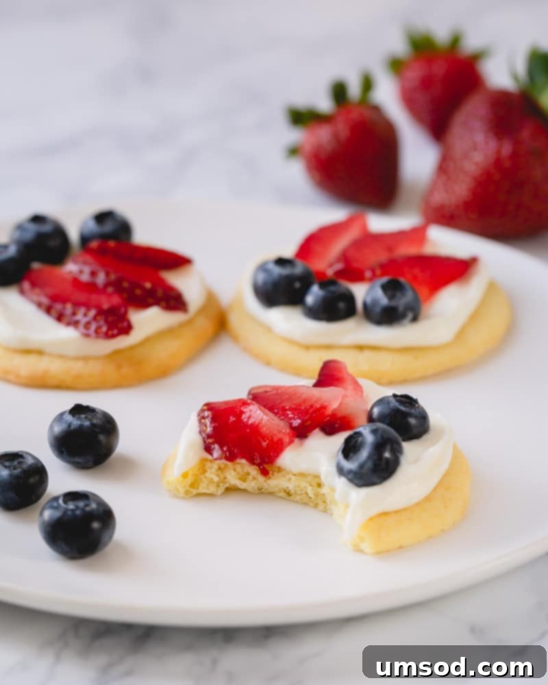 A close-up of mini fruit pizzas, highlighting the creamy white chocolate frosting and colorful fresh fruit toppings. Perfect for any summer occasion.