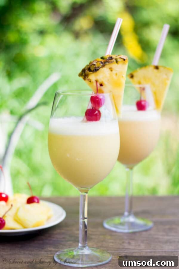 A refreshing orange-kissed Pina Colada served in a glass with a pineapple wedge and cherry garnish