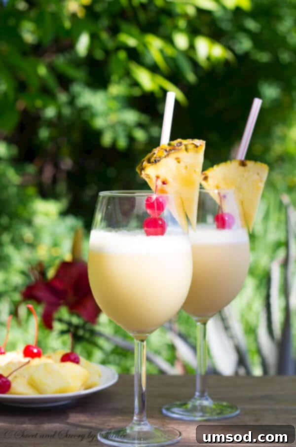 Two glasses of frosty orange Pina Coladas garnished with fresh pineapple wedges and maraschino cherries