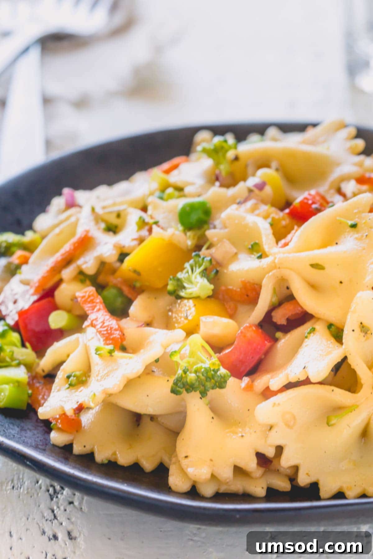 A close-up of colorful farfalle pasta salad, showcasing a variety of fresh vegetables and balsamic dressing.
