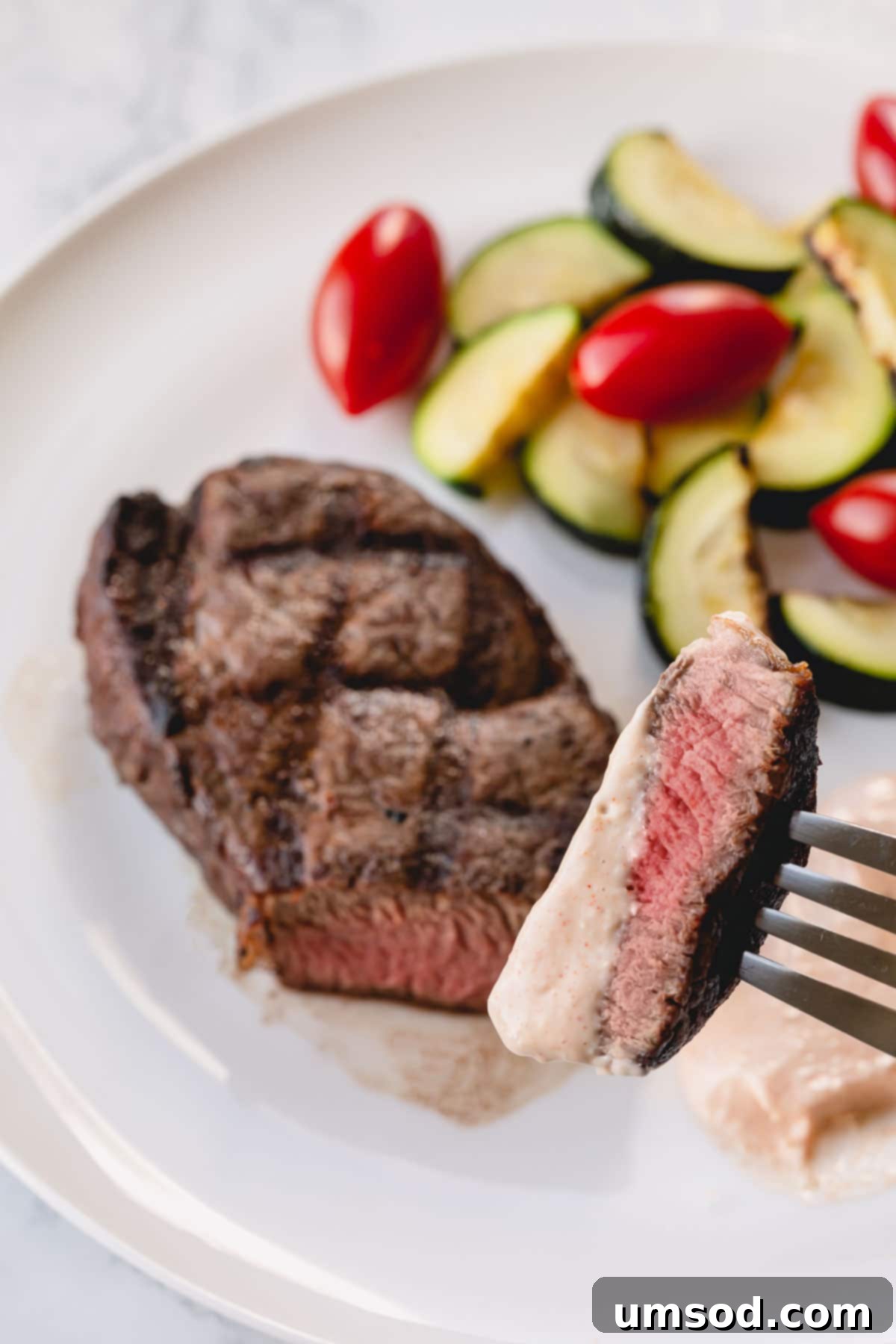 Effortless Grilled Filet Mignon 5 A whole grilled filet mignon on a white plate with zucchini and cherry tomatoes on the side, ready to be enjoyed.
