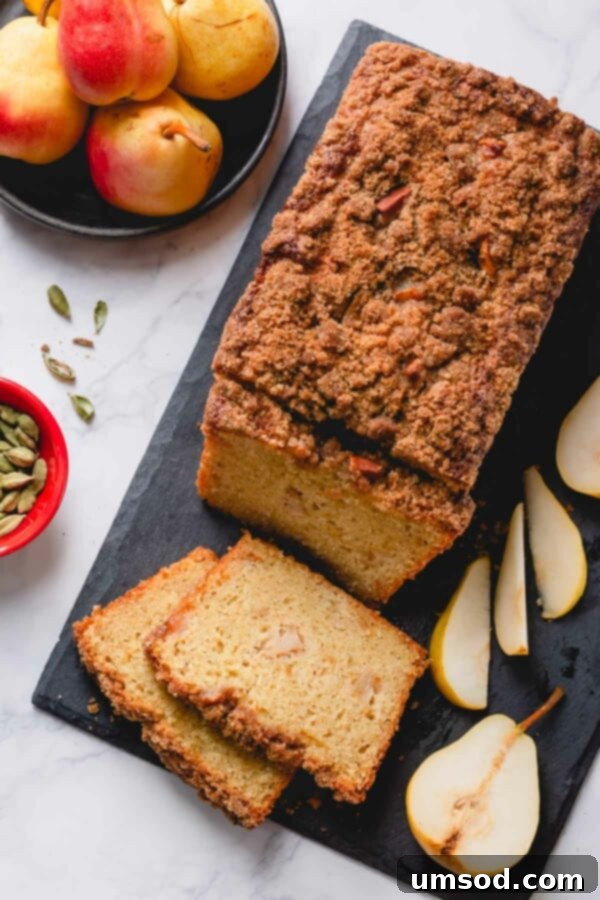 Overhead shot of a perfectly baked caramelized pear quick bread loaf on a black cutting board with several inviting slices ready to be served.
