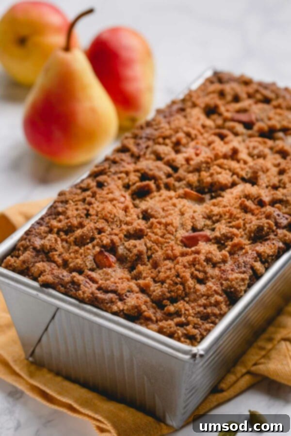 A freshly baked, golden-brown caramelized pear quick bread loaf still in its pan, steam gently rising, showcasing its perfect crust.