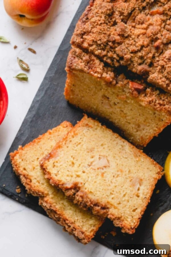 Close-up view of two slices of caramelized pear quick bread, showcasing the moist interior and visible chunks of pear, sitting on a dark cutting board.