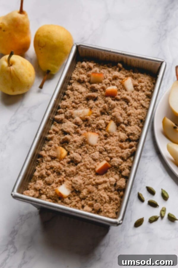 Uncooked pear bread batter in a loaf pan, topped generously with streusel crumbs and fresh pear chunks before baking.