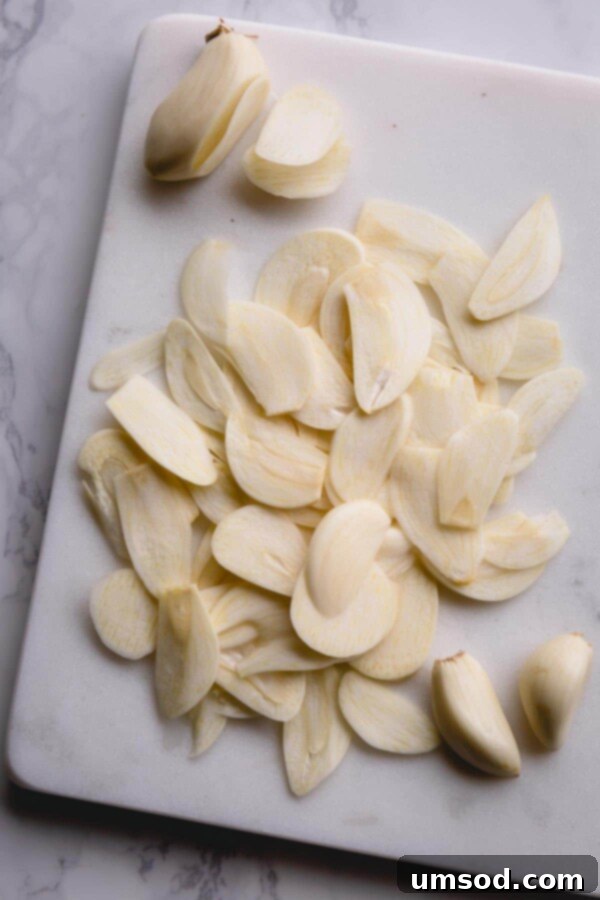 Easy Crispy Garlic Chips 3 Thinly sliced garlic cloves meticulously arranged on a white marble cutting board, ready for frying.