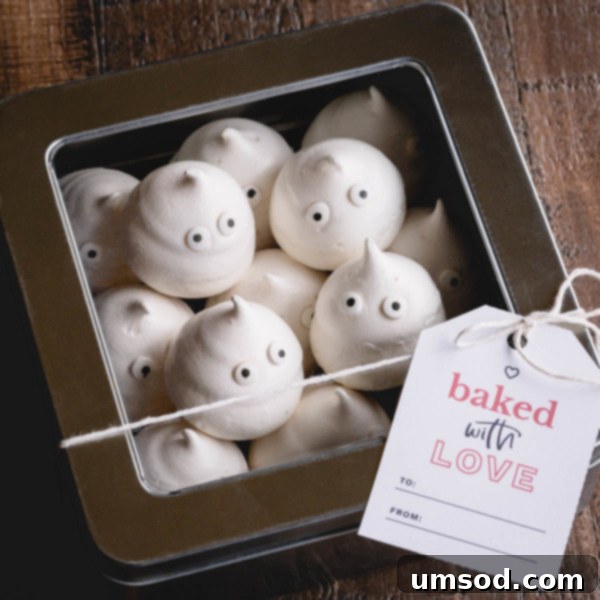 Ghost meringue cookies in a silver box with a window, decorated with a gift tag.