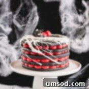 A 5-layer black macaron cake filled with red cream cheese frosting on a white cake stand.