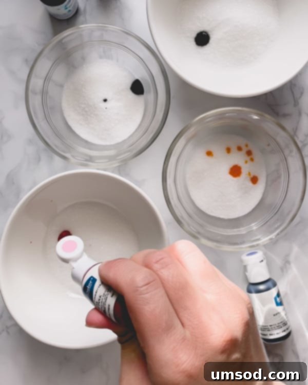 Granulated sugar with droplets of gel food coloring added, ready for mixing.