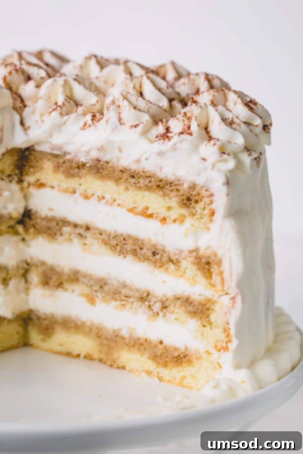 A beautifully presented cut tiramisu layer cake on a white cake platter, showing off the perfectly stacked layers.