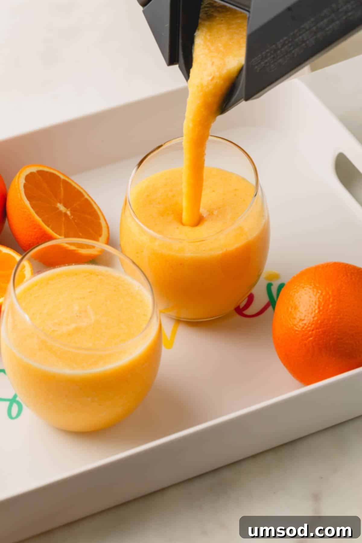 A coconut orange Julius drink being poured into two glasses from a blender.