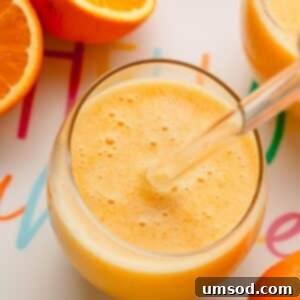 A glass of coconut orange Julius with a glass straw sticking out and oranges around it.