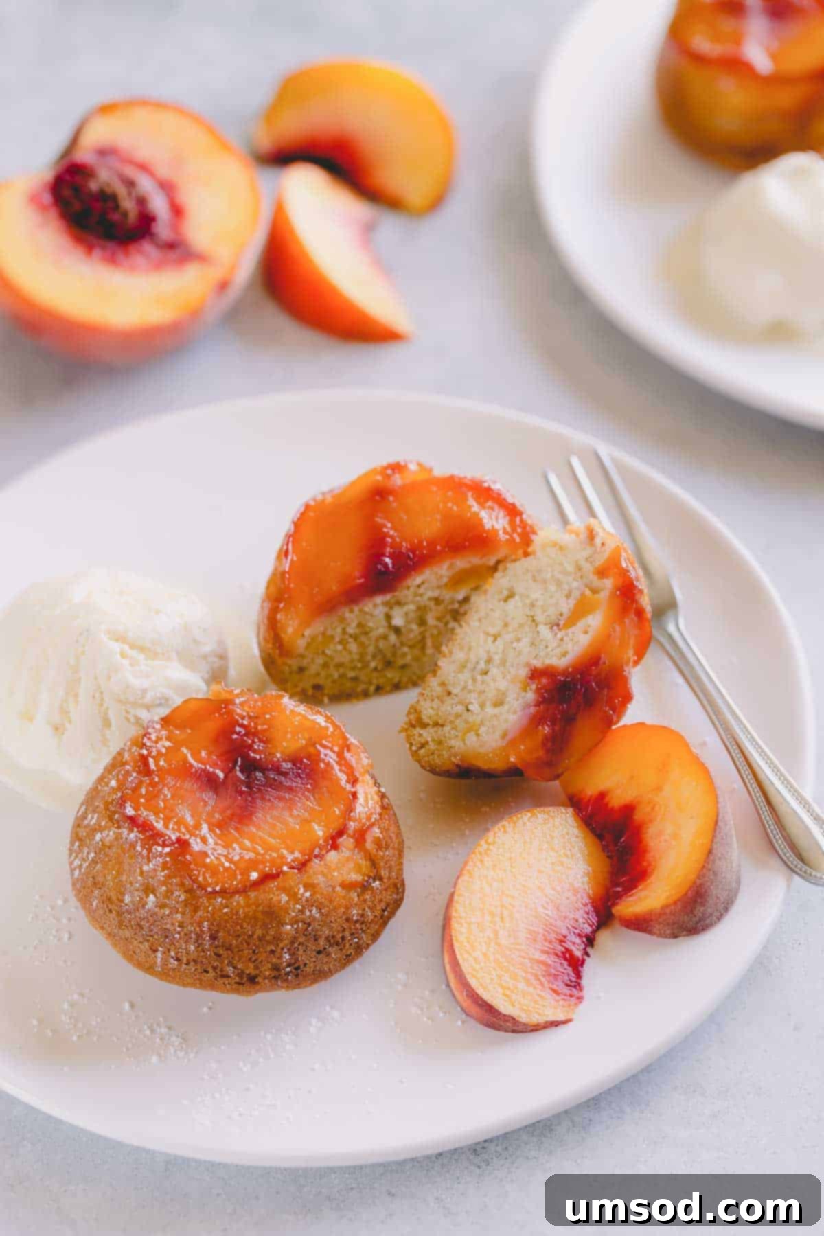 Caramelized Peach Upside-Down Cupcakes 2 Peach upside down mini cakes on a white serving plate with vanilla ice cream and sliced peaches.