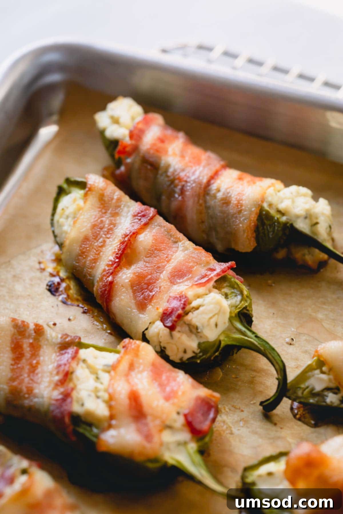 Perfectly cooked bacon wrapped jalapeno poppers arranged on a baking sheet, golden and crispy.