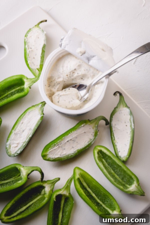 Jalapeno halves generously filled with cream cheese, ready for bacon wrapping.