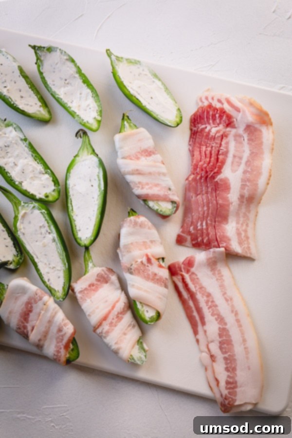 A stuffed jalapeno half being wrapped tightly with a strip of thin-cut bacon.