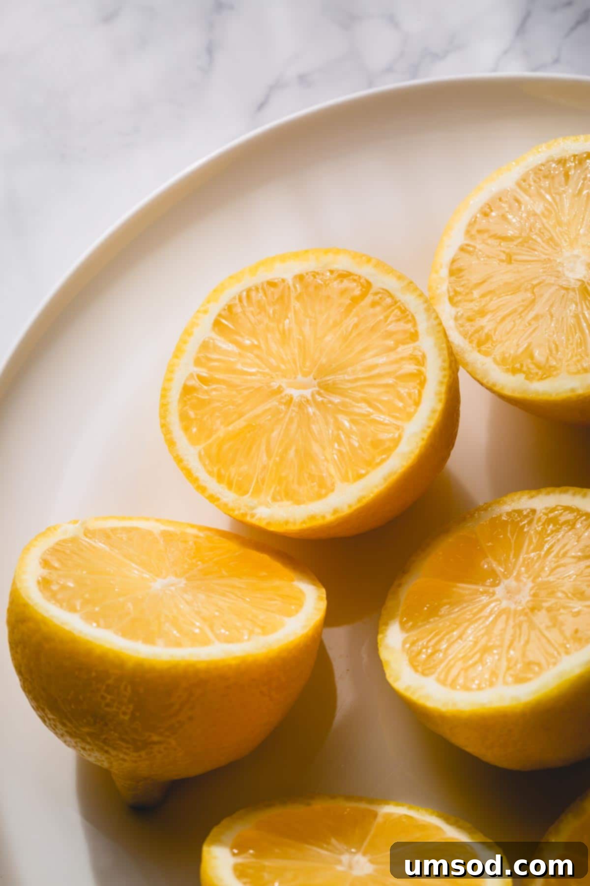 The Ultimate Lemon Handbook 2 Lemon halves on a white plate, vibrant and fresh.