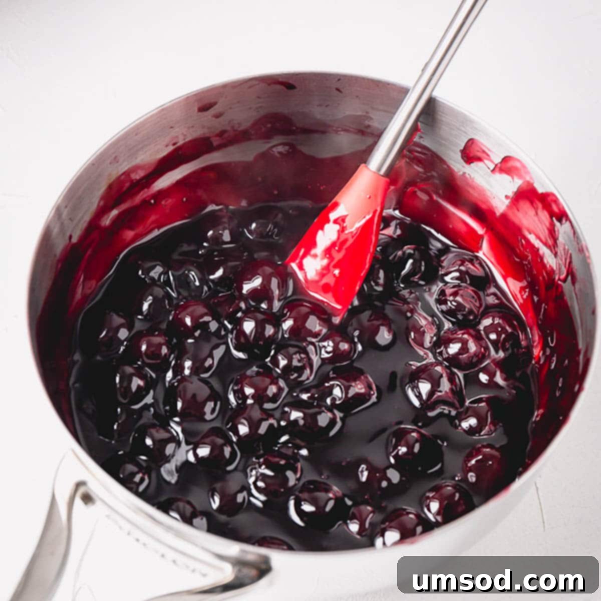 A vibrant homemade cherry pie filling simmering gently in a stainless steel saucepan.