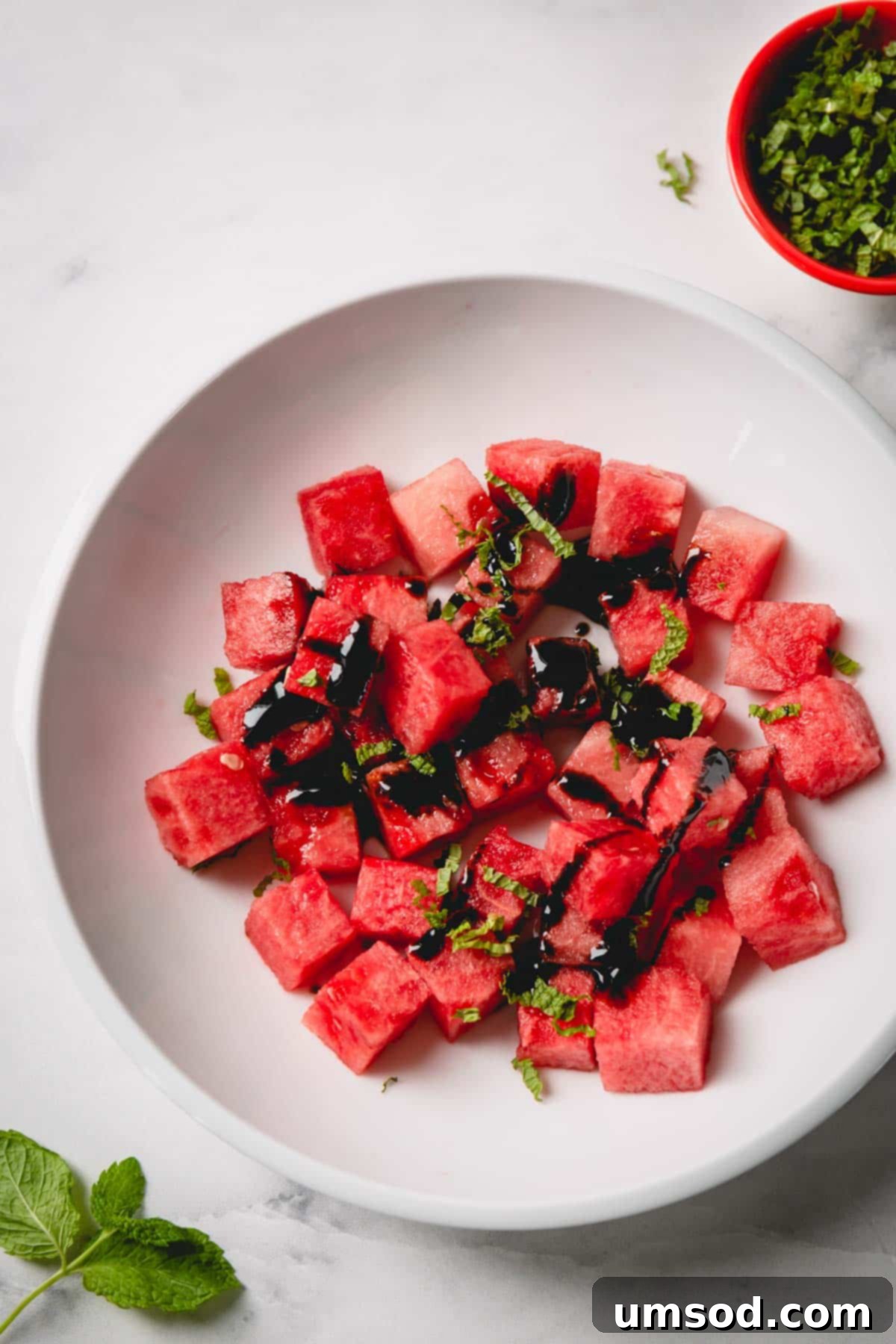 Choose the Best Watermelon Every Time 5 Cubed watermelon in a white bowl topped with balsamic glaze and chopped fresh mint.