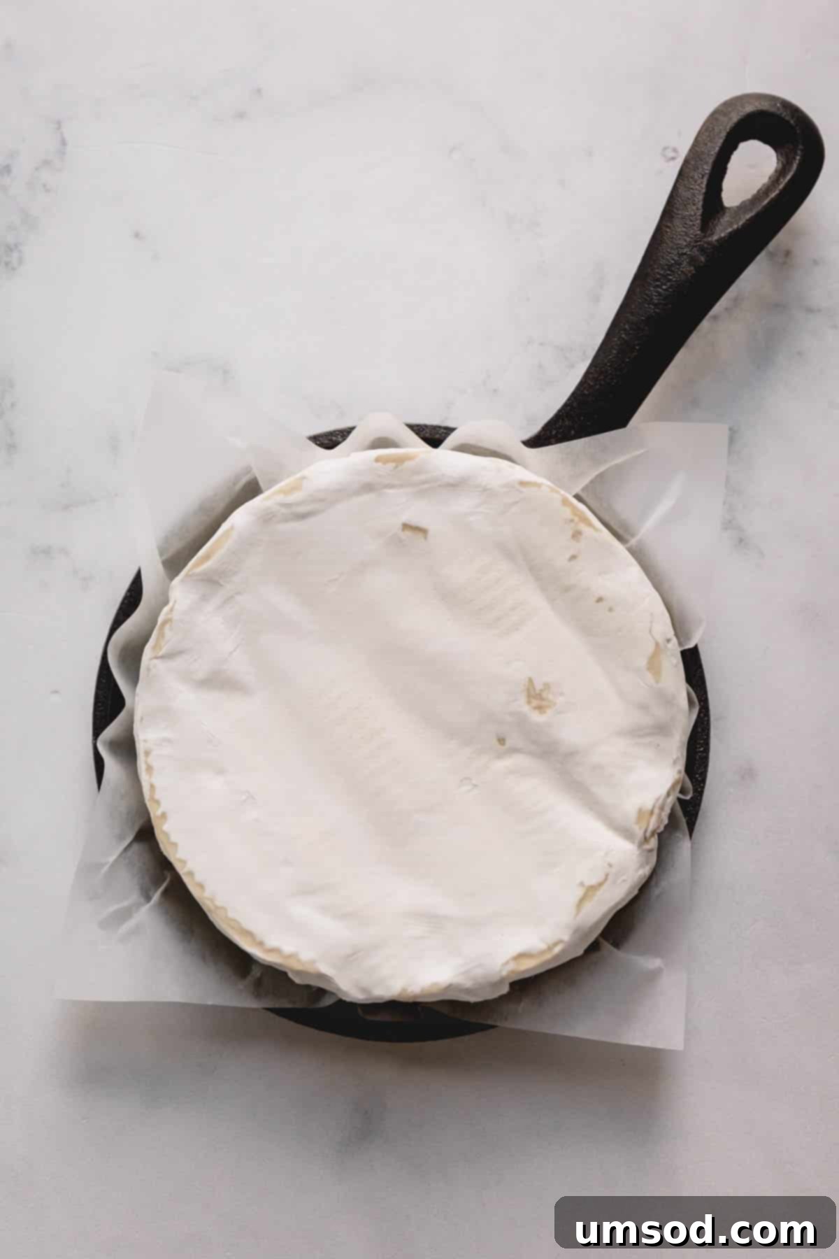 Golden Baked Brie with a Savory Heart 3 A wheel of brie prepared for baking, nestled in a small cast iron skillet lined with parchment paper.