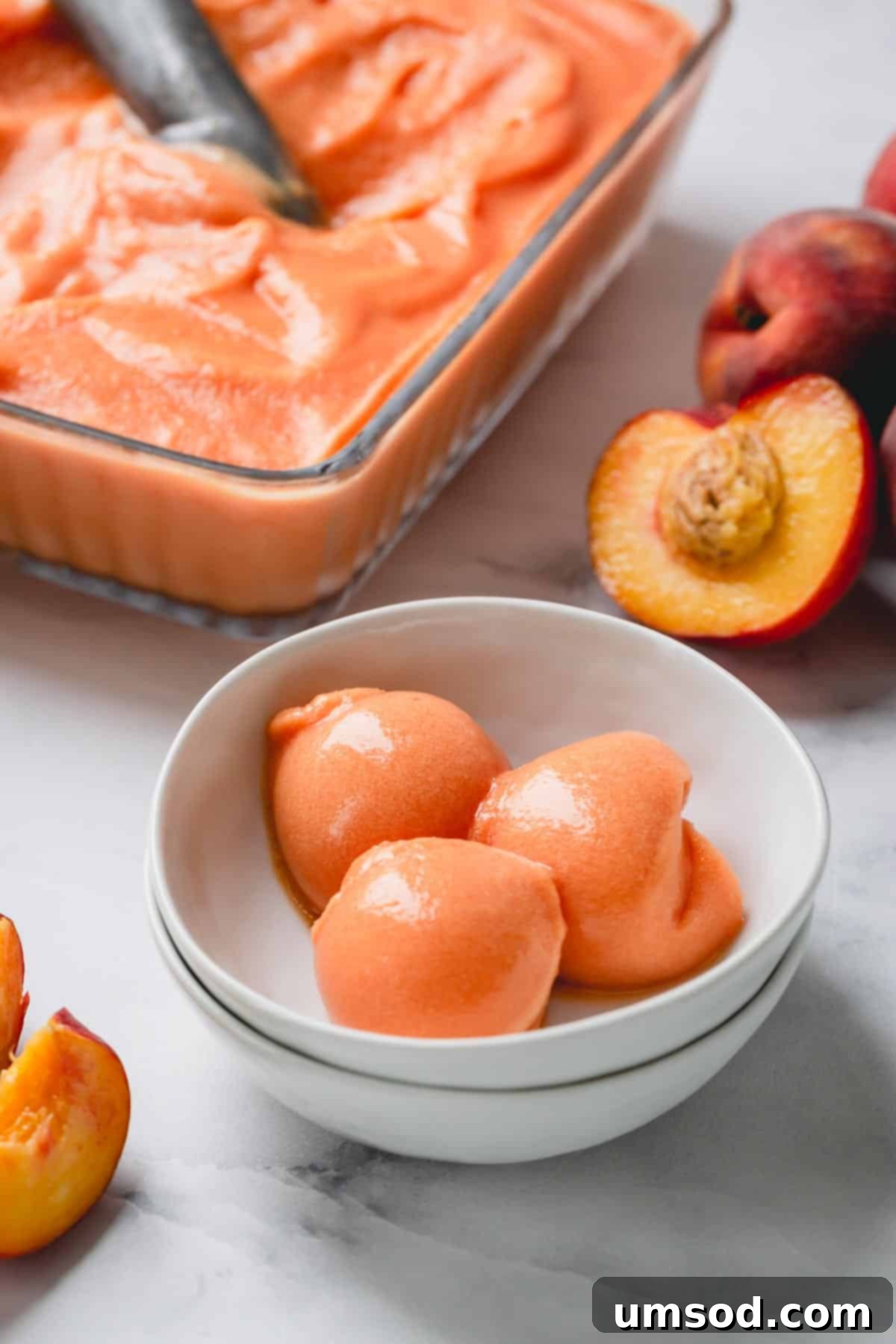 Golden Peach Dream 5 Three perfectly scooped balls of creamy peach ice cream, garnished with fresh mint, in a white bowl, ready to be enjoyed.