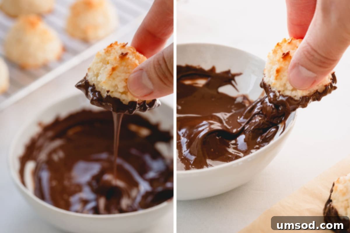 A hand carefully dipping a cooled coconut macaroon into a bowl of perfectly melted, glossy chocolate, illustrating the finishing touch.