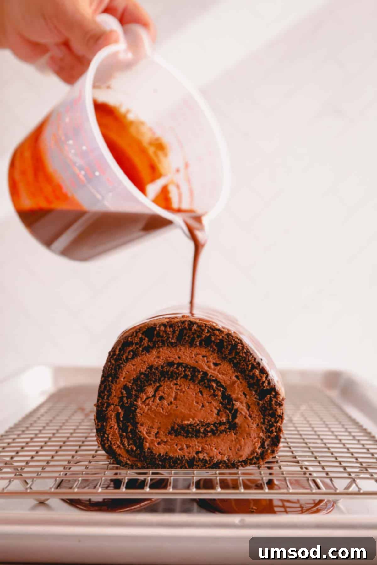 Unapologetically Chocolate Roll Cake 10 A hand gently pouring glossy chocolate ganache over a finished chocolate roll cake, creating an appealing, smooth coating.
