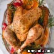 Whole roast turkey on a silver platter garnished with orange slices, pomegranate halves and fresh herbs.