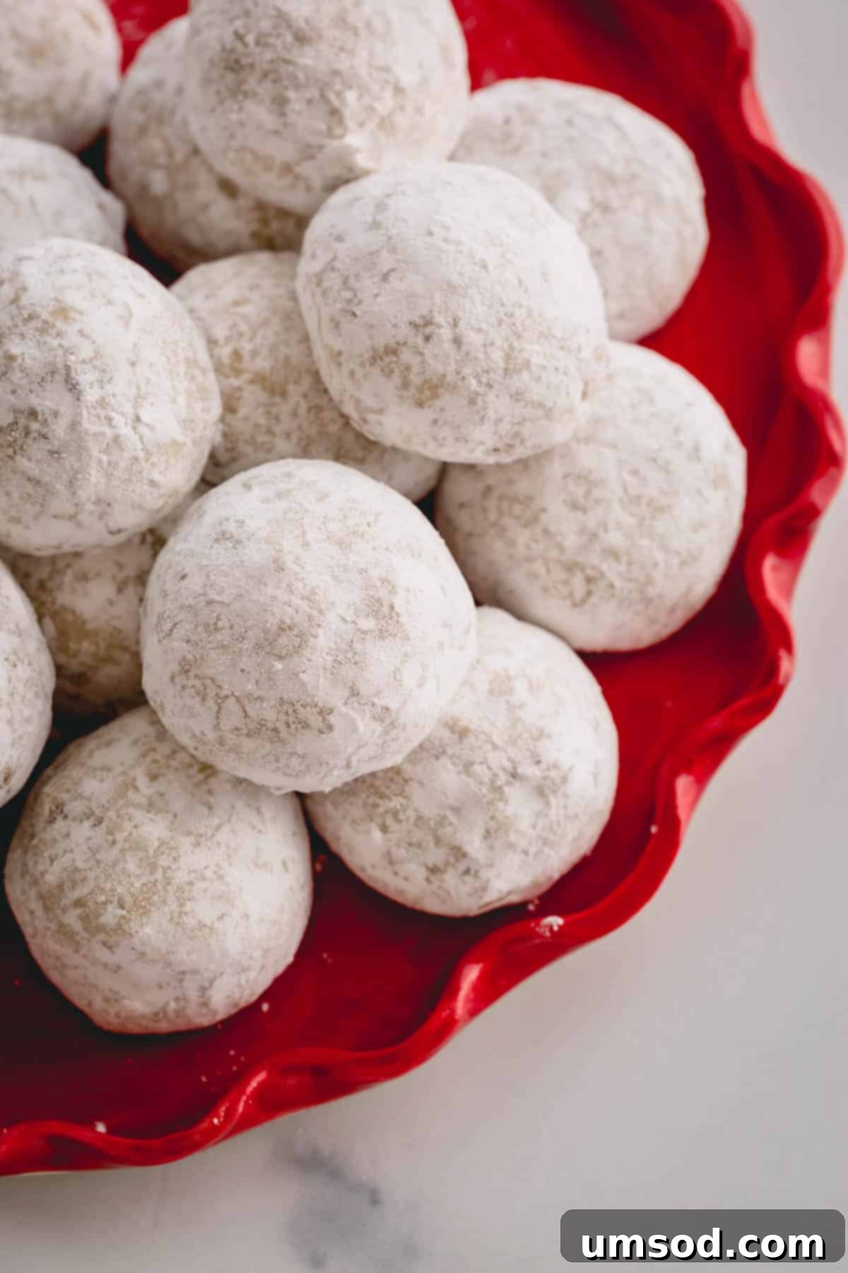 A beautifully arranged plate of freshly baked Russian Tea Cakes, also known as snowball cookies, dusted generously with powdered sugar.