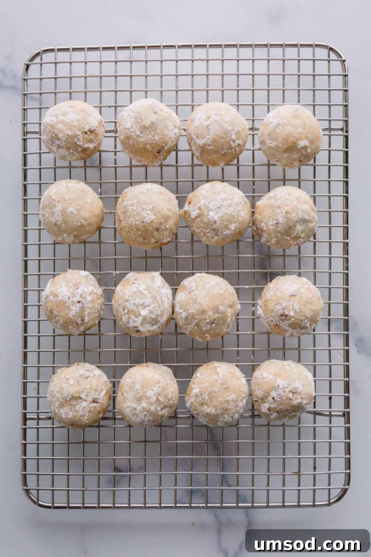 Snowball cookies that have received their first powdered sugar coating, now cooling on a wire rack.