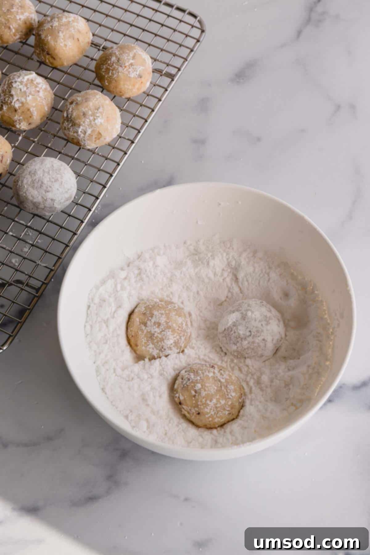 A close-up of snowball cookies perfectly coated in a thick layer of powdered sugar after their second roll, showcasing their pristine white finish.