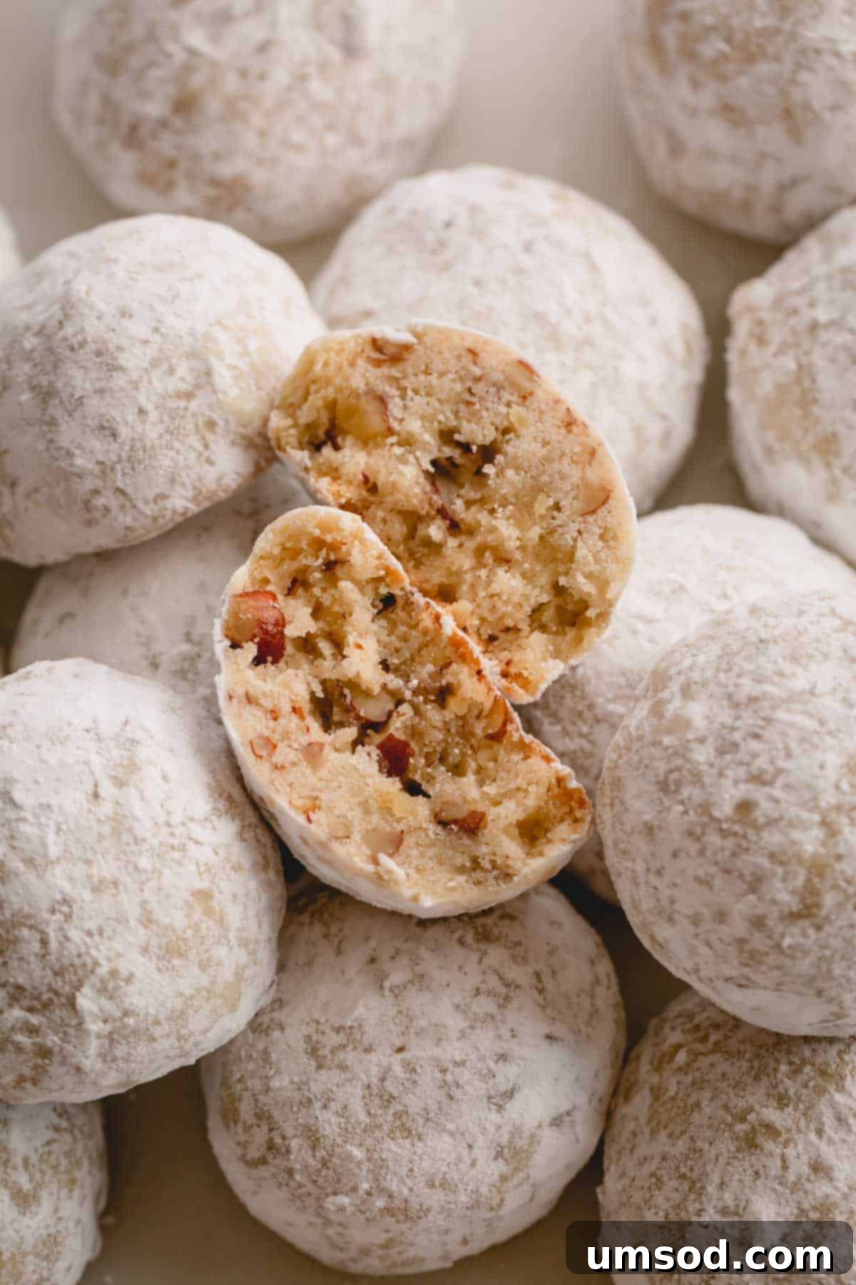A freshly baked Russian Tea Cake cookie, broken in half to reveal its delicate, crumbly texture and bits of toasted pecans inside.