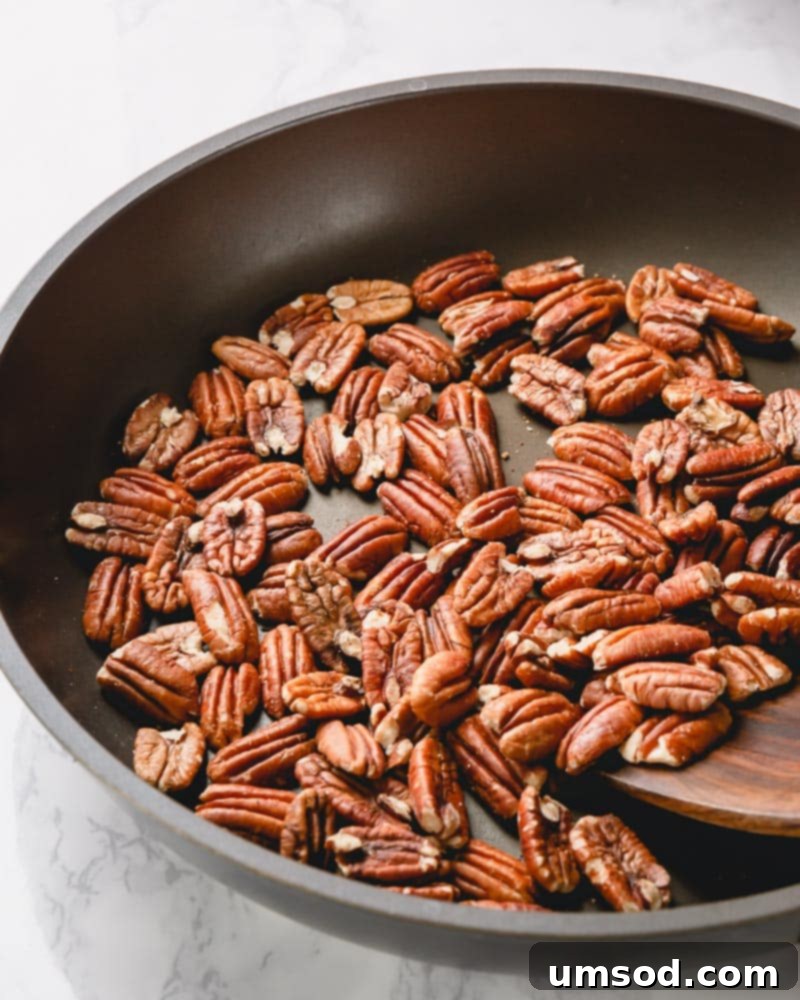 Pecan halves toasting in a large, dry skillet over medium heat.