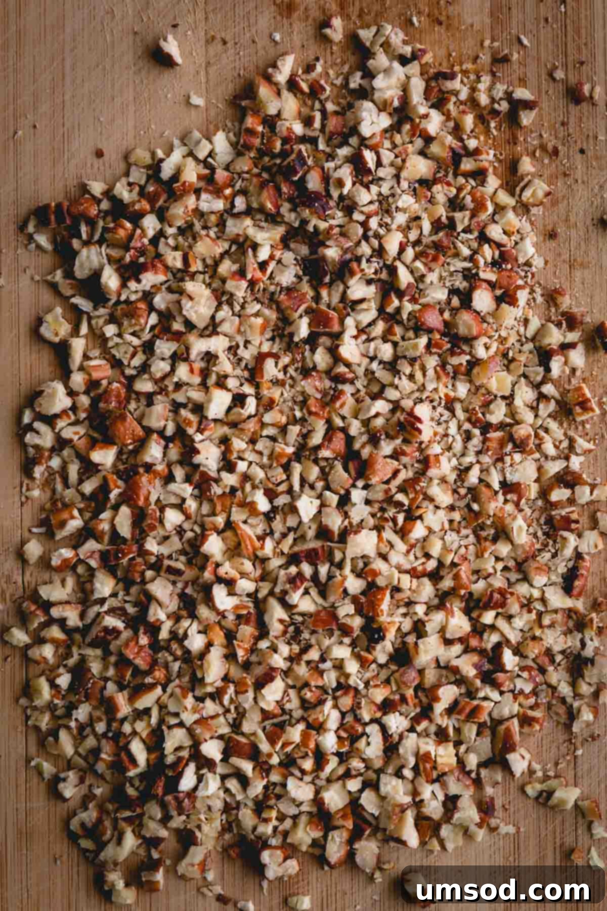 Coarsely chopped toasted pecans on a wooden cutting board, ready to be added to the cookie dough.
