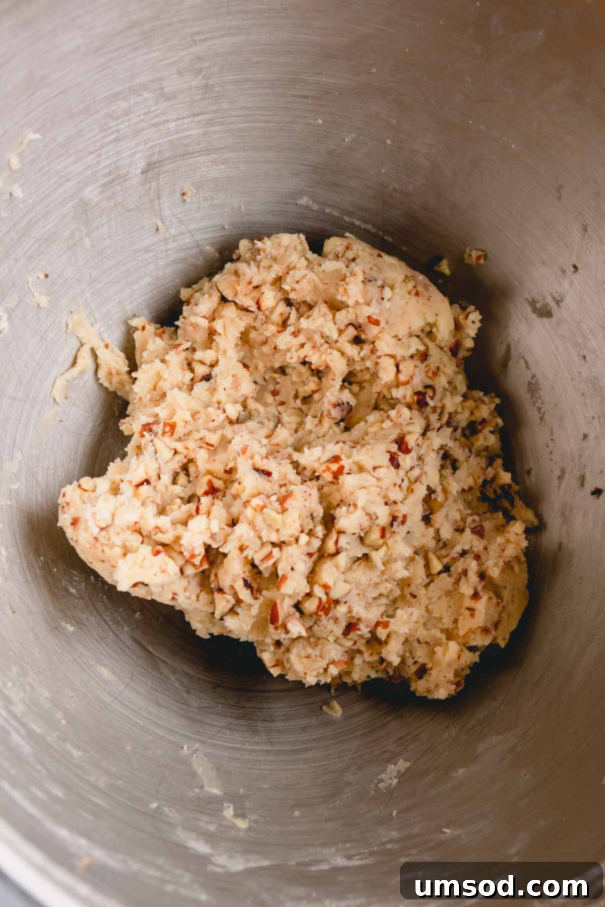 Snowball cookie dough with chopped pecans mixed in, ready for shaping, inside a large mixing bowl.