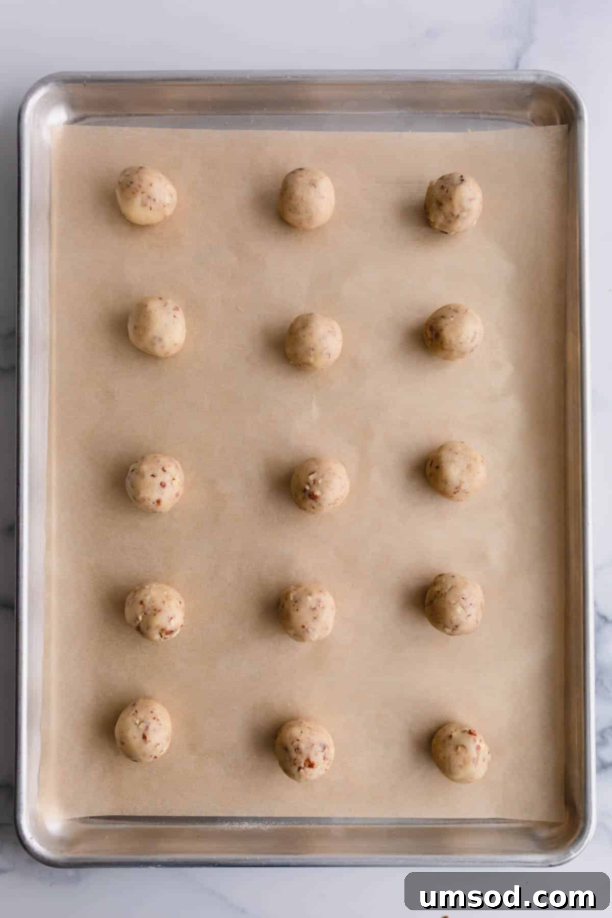 Uniform snowball cookie dough balls neatly arranged on a parchment-lined baking sheet, ready for baking.