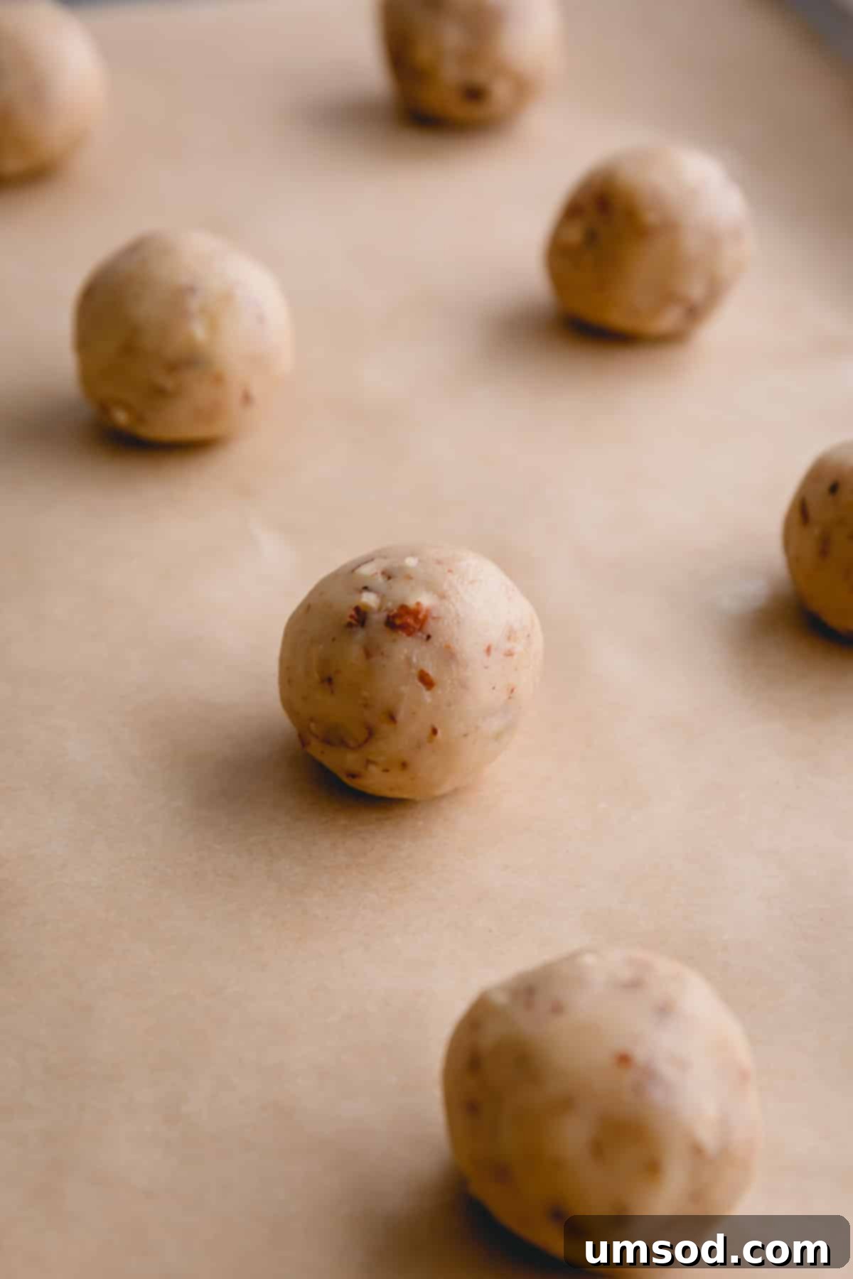 Close-up of perfectly shaped snowball cookie dough balls before baking, showing the incorporation of pecans.