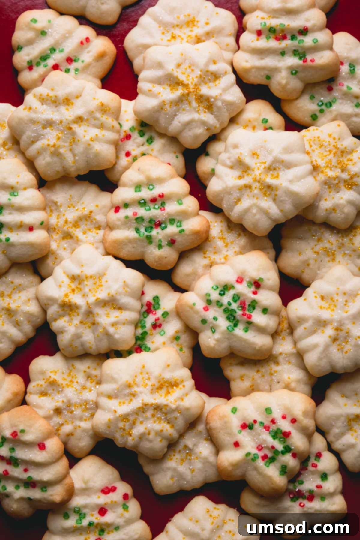 A stack of freshly baked, holiday-shaped spritz cookies, highlighting their delicate patterns.