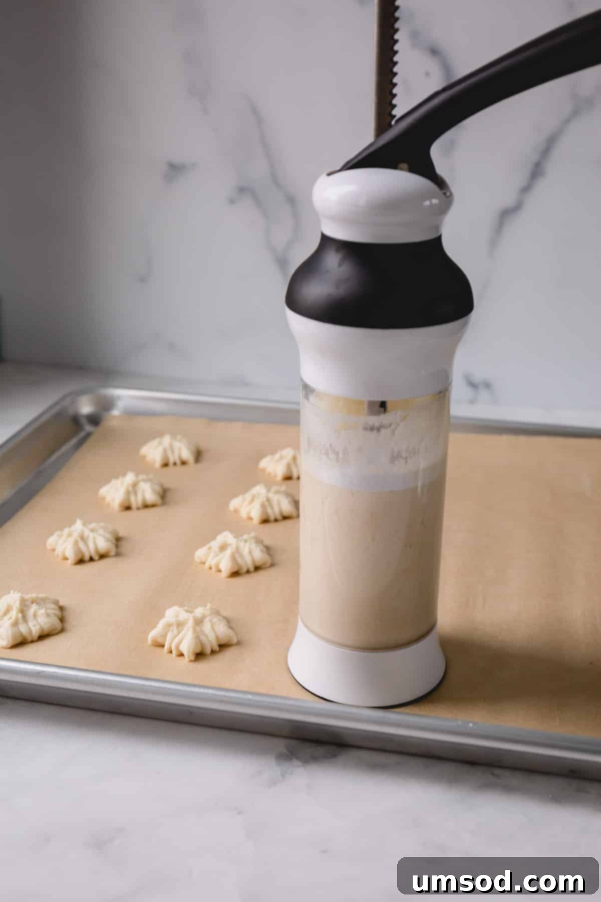 A cookie press in action, pressing spritz cookies onto a baking sheet, illustrating the shaping process.