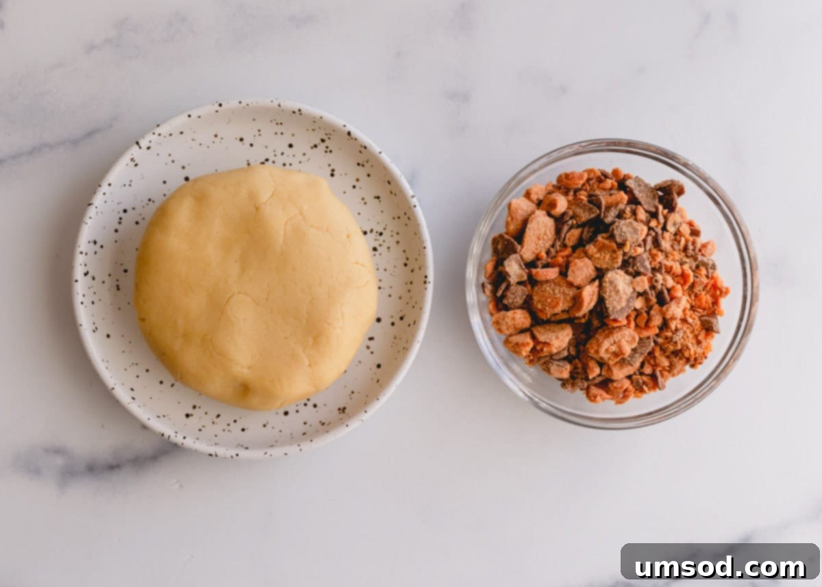 Tek Hamurdan 6dan Fazla Lezzet: Efsanevi Tereyağlı Kurabiye Hamuru 14 A ball of cookie dough alongside a bowl of crushed Butterfinger candy pieces, ready for mixing into cookie bars.