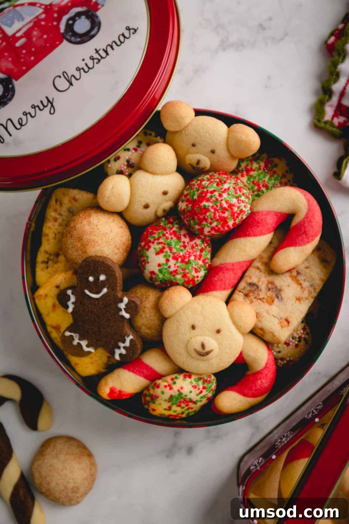 Tek Hamurdan 6dan Fazla Lezzet: Efsanevi Tereyağlı Kurabiye Hamuru 20 A festive round tin can filled to the brim with an assortment of various homemade Christmas butter cookies, perfect for gifting.